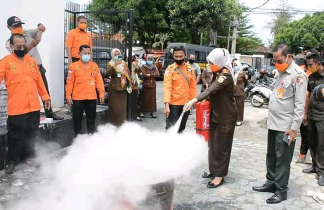 
 caption foto : Kajari Lampura Atik Rusmiati Ambarsari didampingi Kepala BPBD Karim SR, memadamkan kobaran api dalam simulasi cepat tanggap darurat pemadam api, dihalaman kantor Kejari, Selasa (22/9)