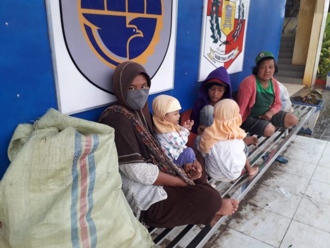 
 caption foto : Dewi Nopasari (28) bersama dua anaknya saat berteduh di halte depan kantor Pemkab Lampura, Kamis (28/1)  