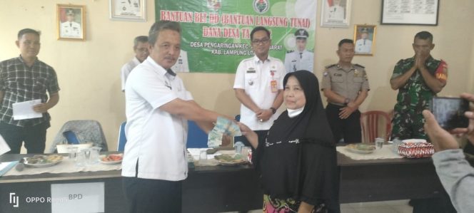 
 Kades Pengaringan Sarkasi, disaksikan Camat Abung Barat Gunaido Uthama, Bhabinkamtibmas Aipda Polisi Meiji, dan Babinsa Serda Sutrisno, saat menyerahkan BLT DD kepada KPM di Kantor Desa Setempat, Rabu(29/6).Foto Riduan Radar Kotabumi 
